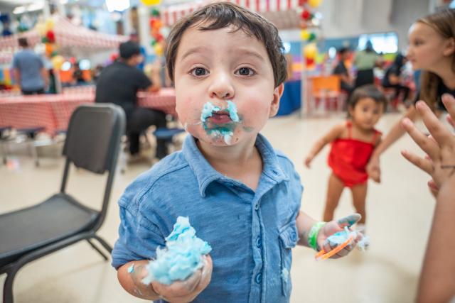 A young boy at the carnival enjoys cotton candy which has smudged all over his face.