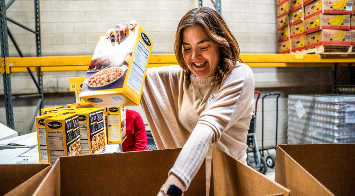 Volunteer packs a food box with boxes of cereal.
