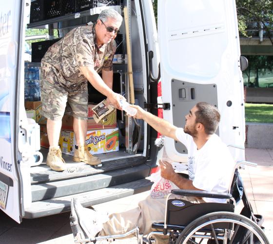 Older man in the back of a van handing a water bottle to man in a wheelchair