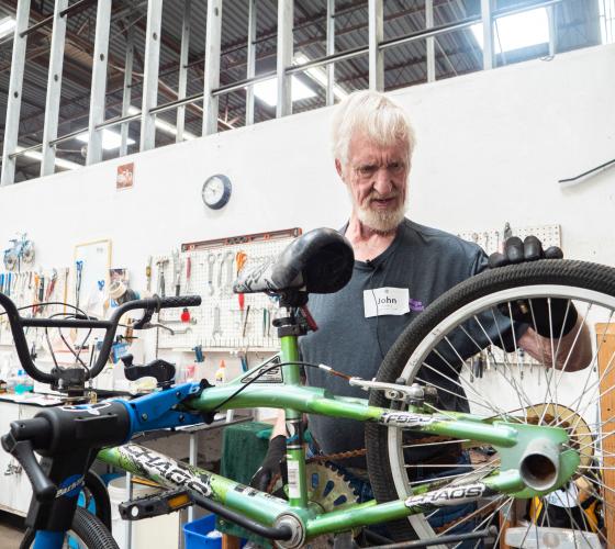 Bike Shop Volunteer Header Man checking the wheel of a bike