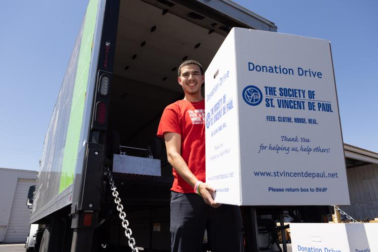 Man holding a food drive donation box on the back of on SVdP truck