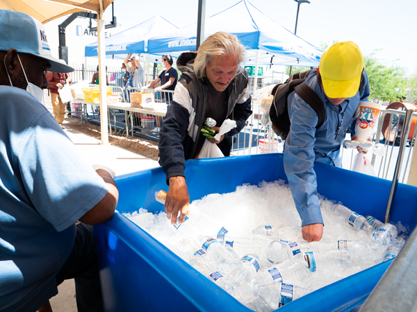 Two men grabbing water bottles out of a container of ice