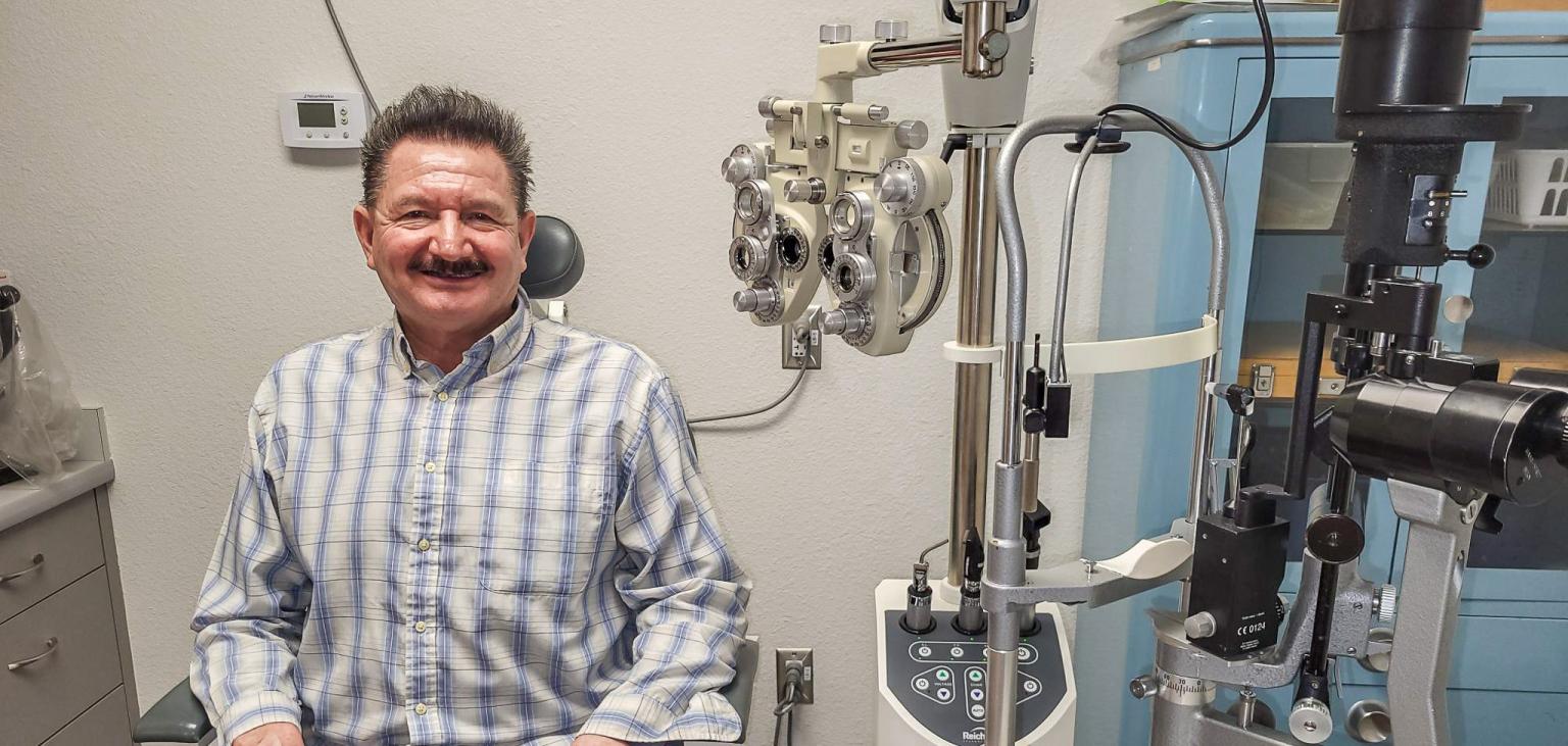 Francisco sits in a medical clinic chair with the optometrists instruments next to him.