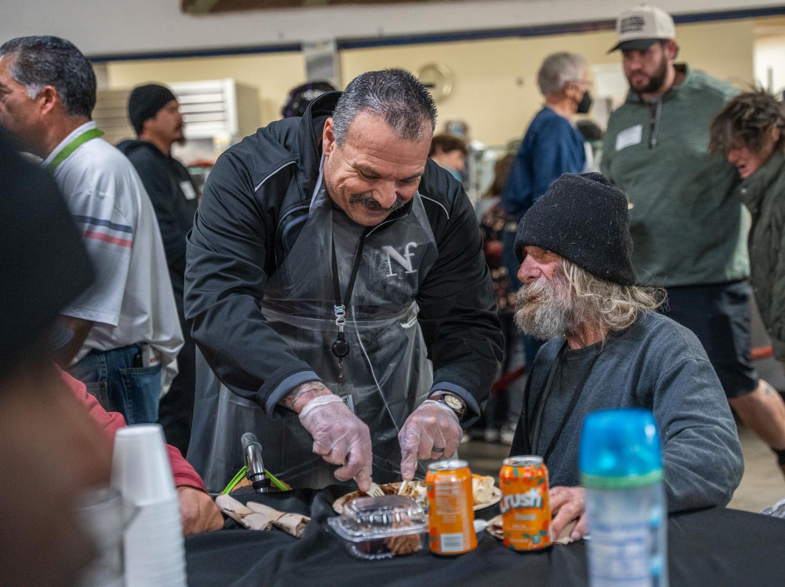 A volunteer cuts a steak for a guest at SVdP's Phoenix Dining Room.