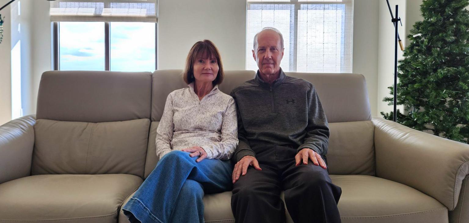 Cathy and her husband sit in their living room.