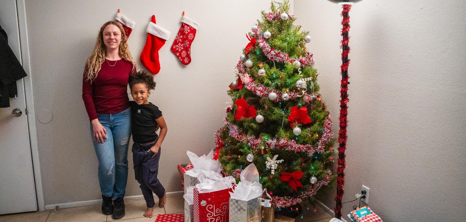 Christin and Keira stand next to their tree with new presents under.