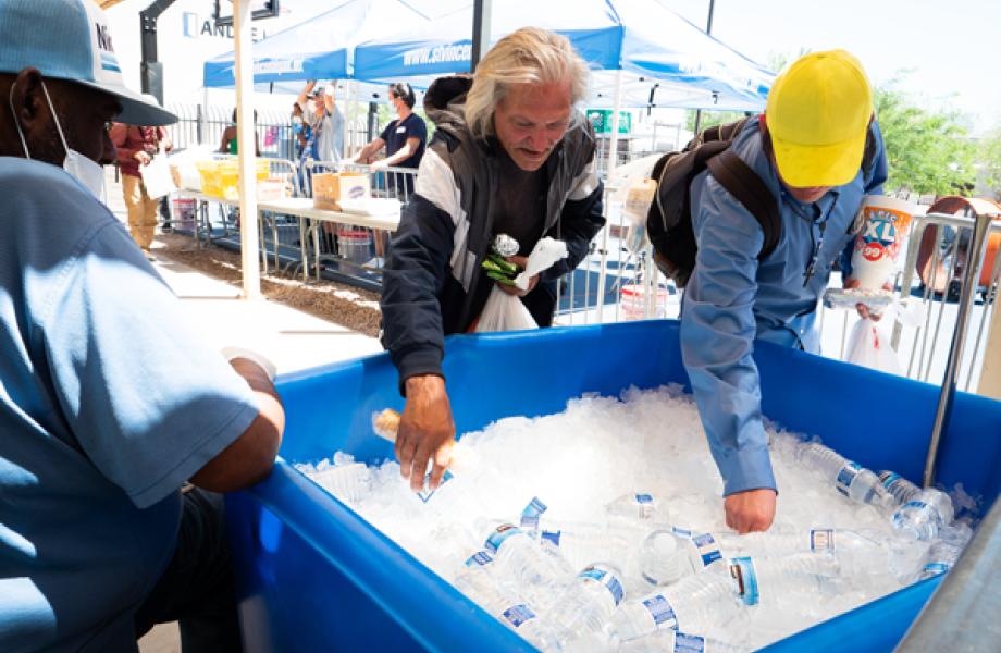 Two men grabbing water bottles out of a container of ice