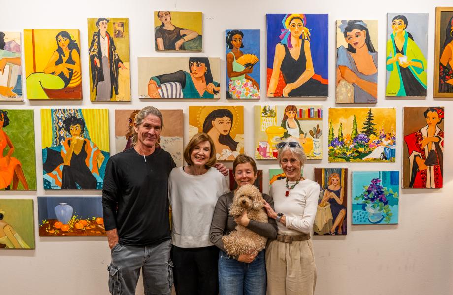 Most of the team behind the painting-donation project stands before a wall covered in paintings.