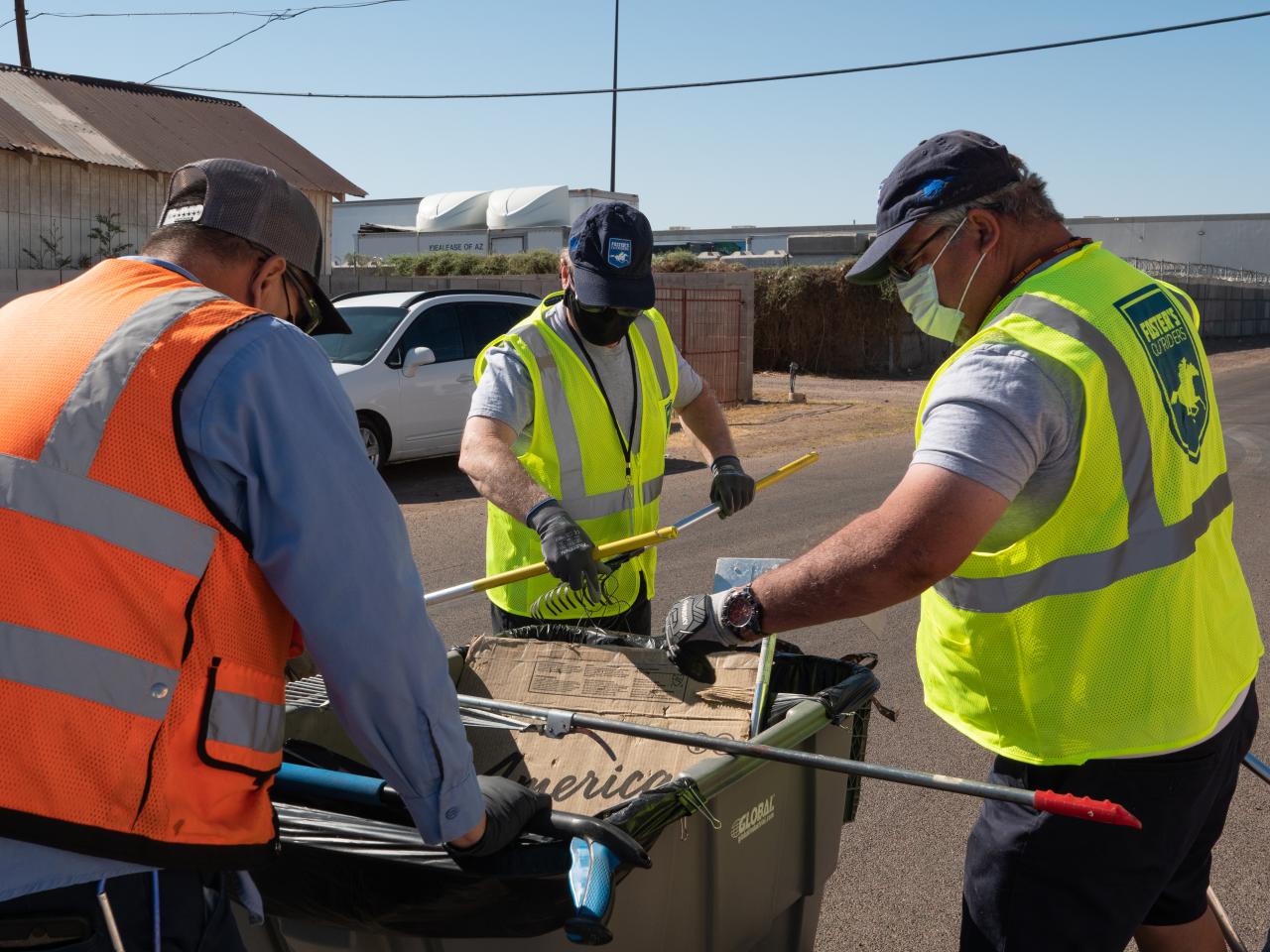 A group of men throwing trash from the street into a bin