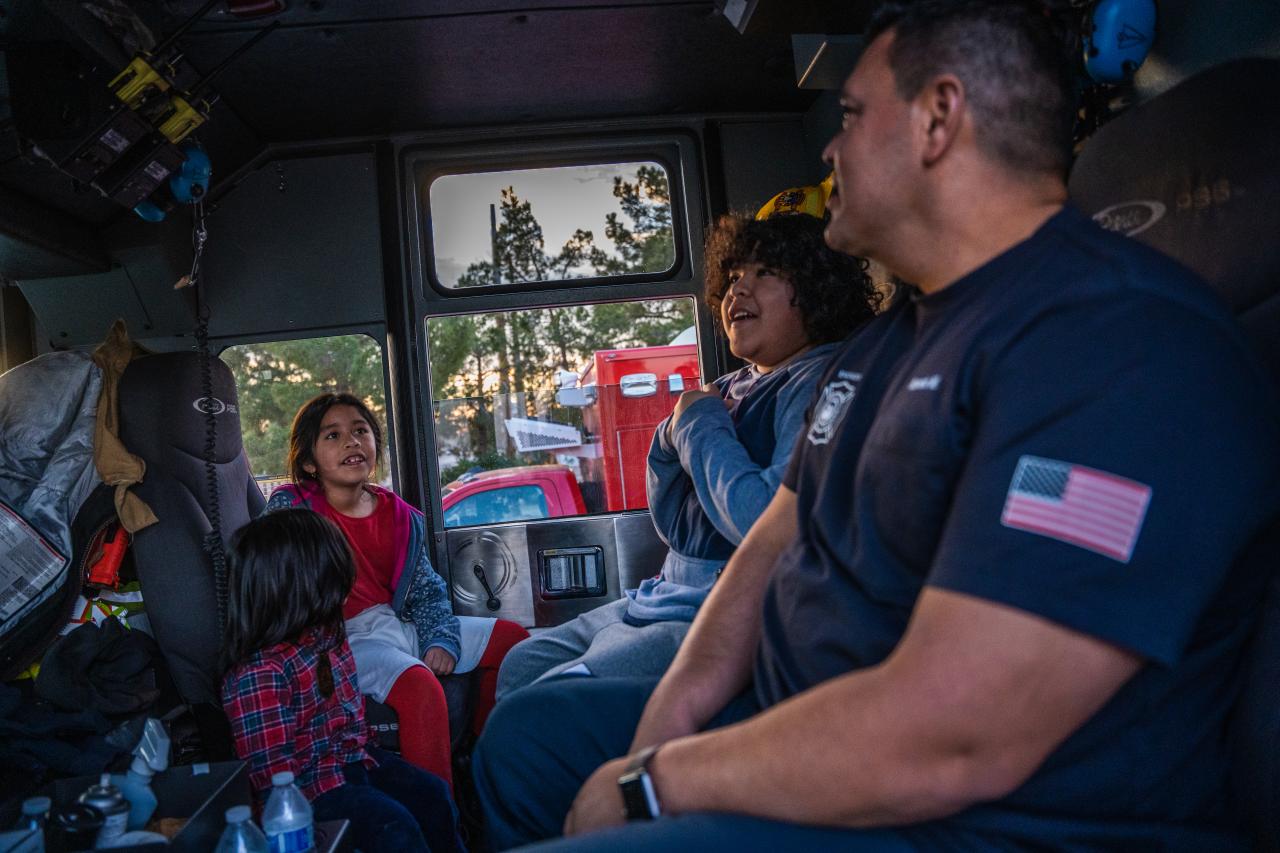 The kids sit in the cab of the fire engine with one of the firefighters.