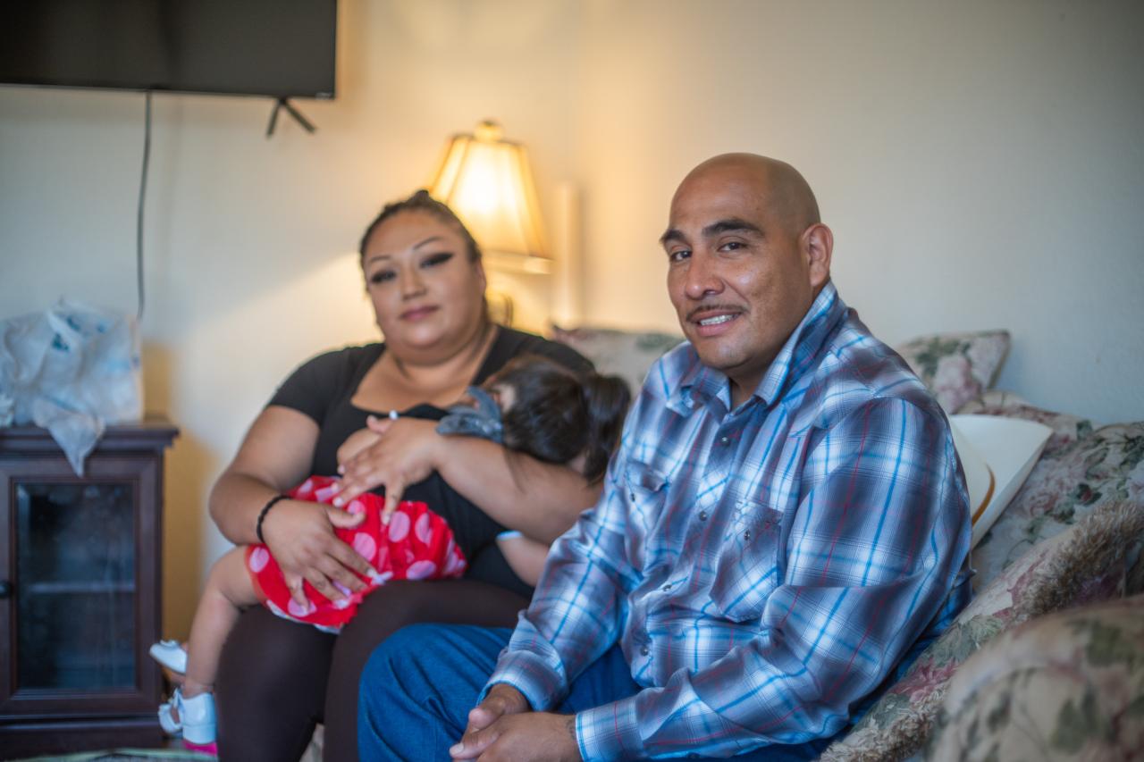 Julio sits in the living room of his new apartment with his wife and one of his children.
