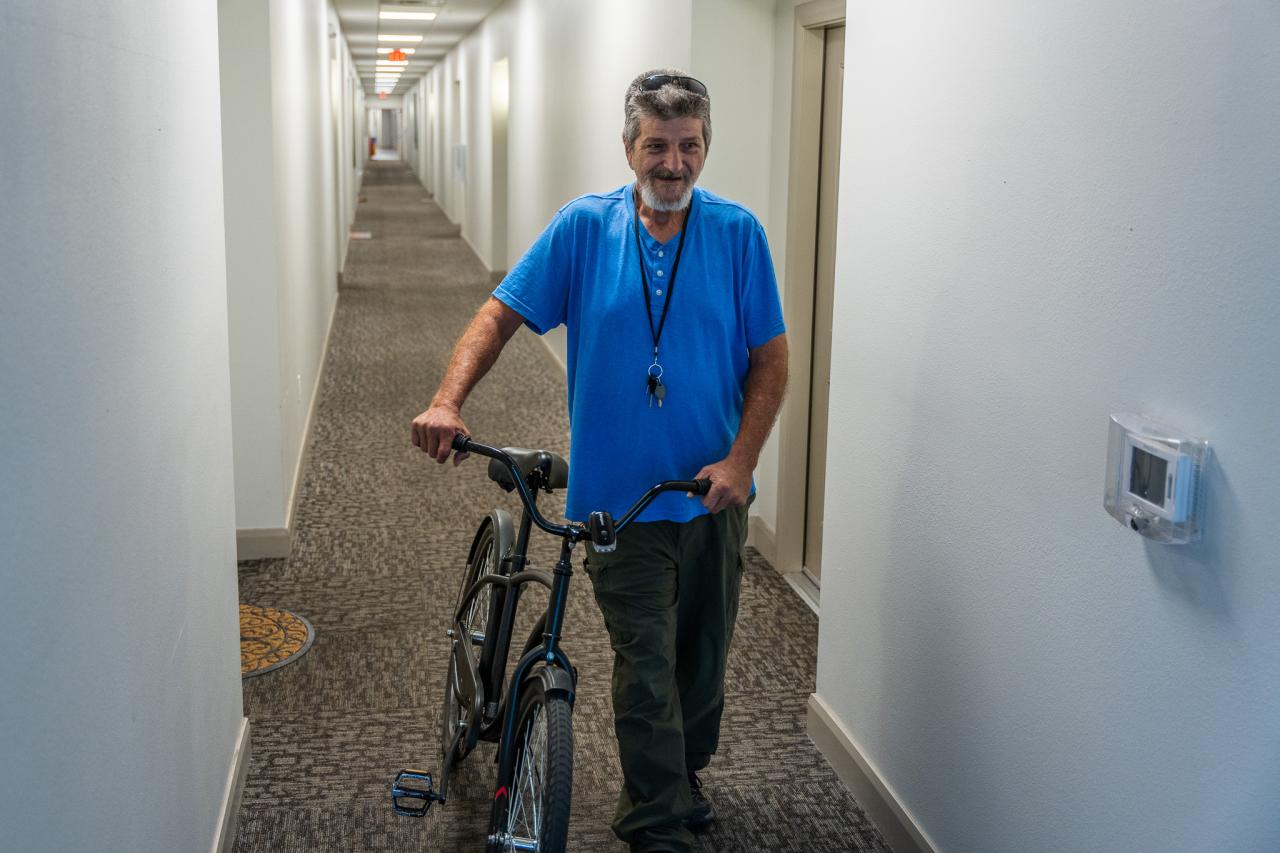 Kenneth walks his bike down the hall.